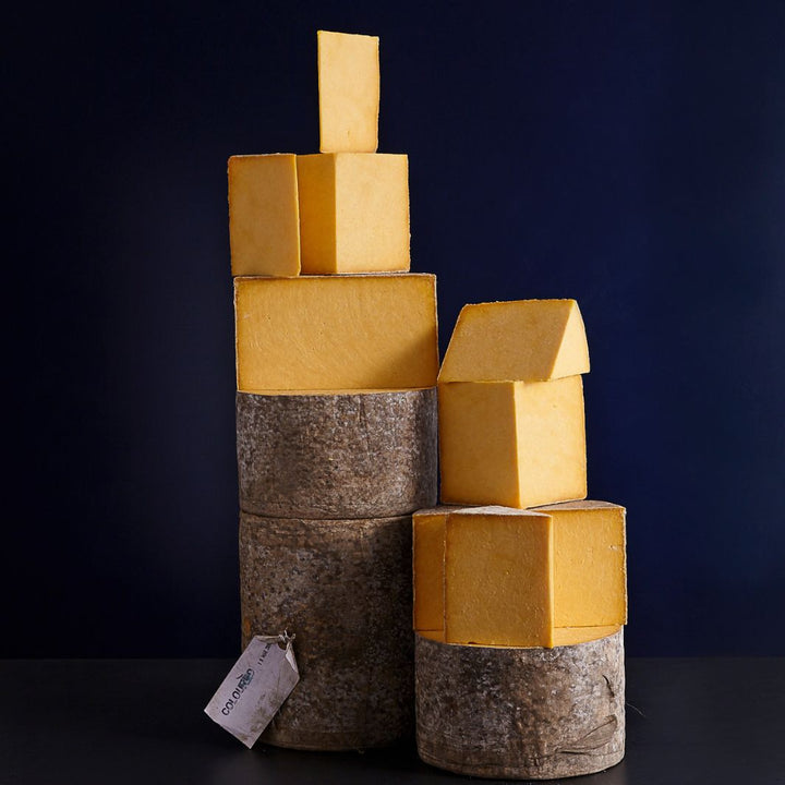 Towers of whole and cut pieces of orange coloured Appleby’s Cheshire cheese which is cloth-bound with a crumbly paste