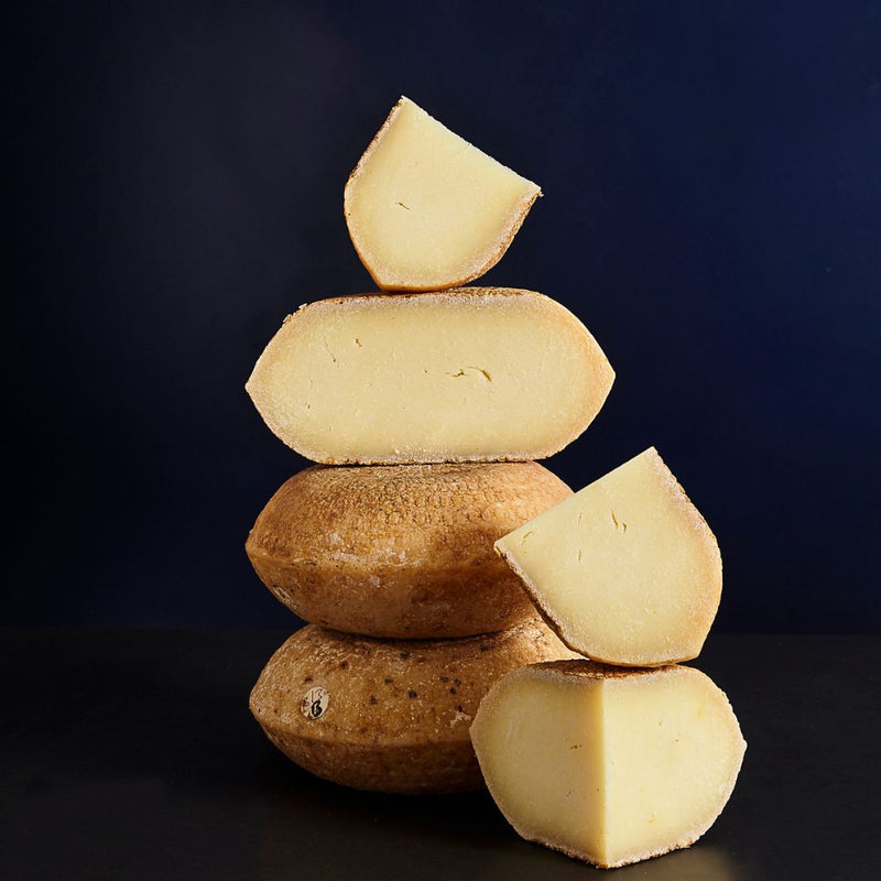 Tower of whole and cut pieces of Berkswell sheep’s milk cheese with a firm off-white coloured paste