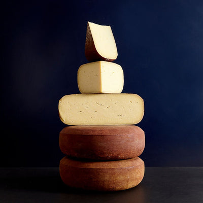 Various sized cut pieces sat on whole Doddington raw cow’s milk cheeses showing the firm, cream-coloured, smooth paste and red rind
