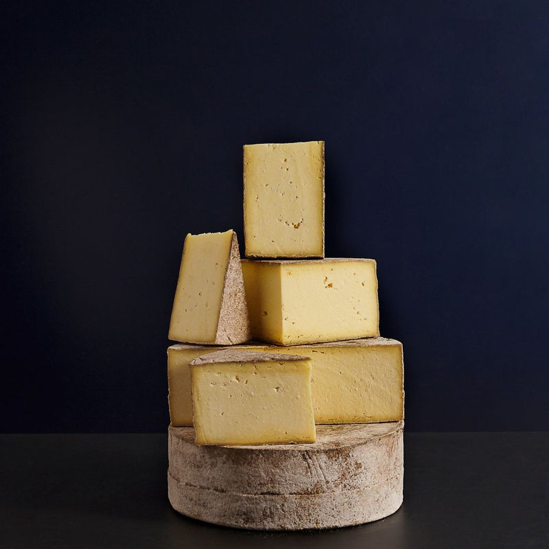 Various sized cut pieces sat on a whole Duckett’s Caerphilly raw cow’s milk cheese, showing the crumbly curd paste and edible natural rind