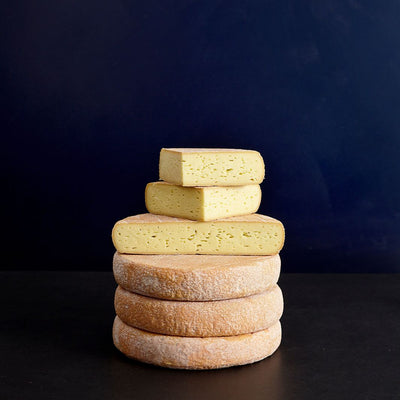 Tower of whole and cut pieces of Durrus washed rind cow’s milk cheese, showing the patterned pinky rind and soft, creamy-coloured paste