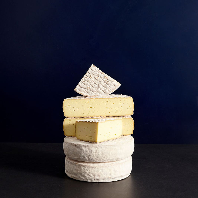 Tower of whole and cut pieces of Gubbeen semi-soft washed rind cow’s milk cheese, showing the patterned rind and creamy-coloured paste