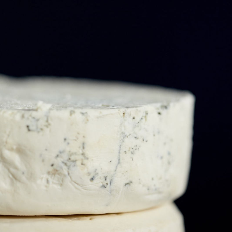 Close up of a cut piece of Harbourne Blue vegetarian goat’s milk cheese showing the light blue veining and a crumbly texture