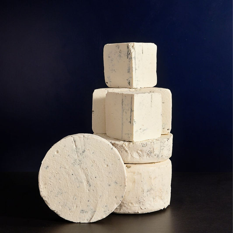 Tower of whole and various sized cut pieces of Harbourne Blue vegetarian goat’s milk cheese with light blue veining and a crumbly texture