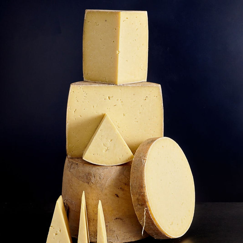 Tower of whole and smaller cut pieces of cloth-bound Isle of Mull Cheddar cheese with a firm close-textured paste