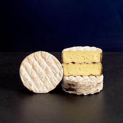 Pile of whole and cut washed rind Little Rollright cow’s milk cheeses, with a soft paste and wrapped in a band of spruce bark