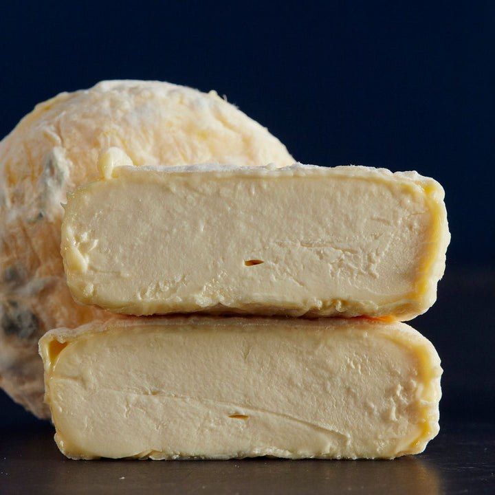 Close up of a whole and cut St Jude cow’s milk cheese with mould-spots on the creamy-coloured wrinkly rind and a light, fluffy, mousse-like paste