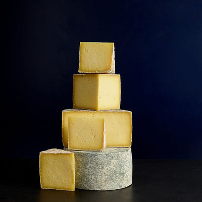 Various sized cut pieces sat on a whole Whin Yeats Wensleydale raw cow’s milk cheese showing the golden-coloured paste and grey rind