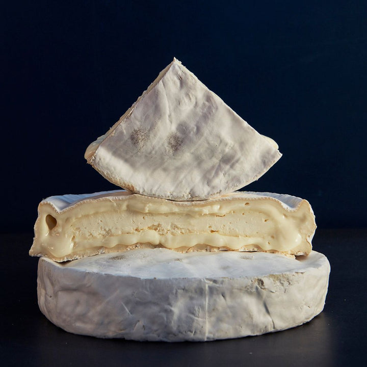 Two cut pieces on a whole Wigmore vegetarian sheep’s cheese, showing the creamy, soft paste beneath the natural, white rind