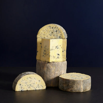 Group of a whole and cut pieces of Cashel Blue vegetarian cow’s milk cheese, showing the blue veining, delicate natural rind and rich, buttery paste