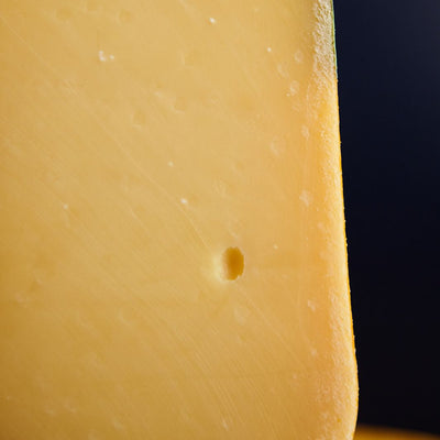 Close up of a cut piece of Coolea Gouda-like cow’s miIk cheese, showing the rind and firm, smooth, closely textured paste