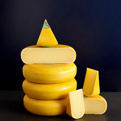 Tower of whole and cut pieces of Coolea Gouda-like cow’s miIk cheese, showing the firm, smooth and closely textured paste