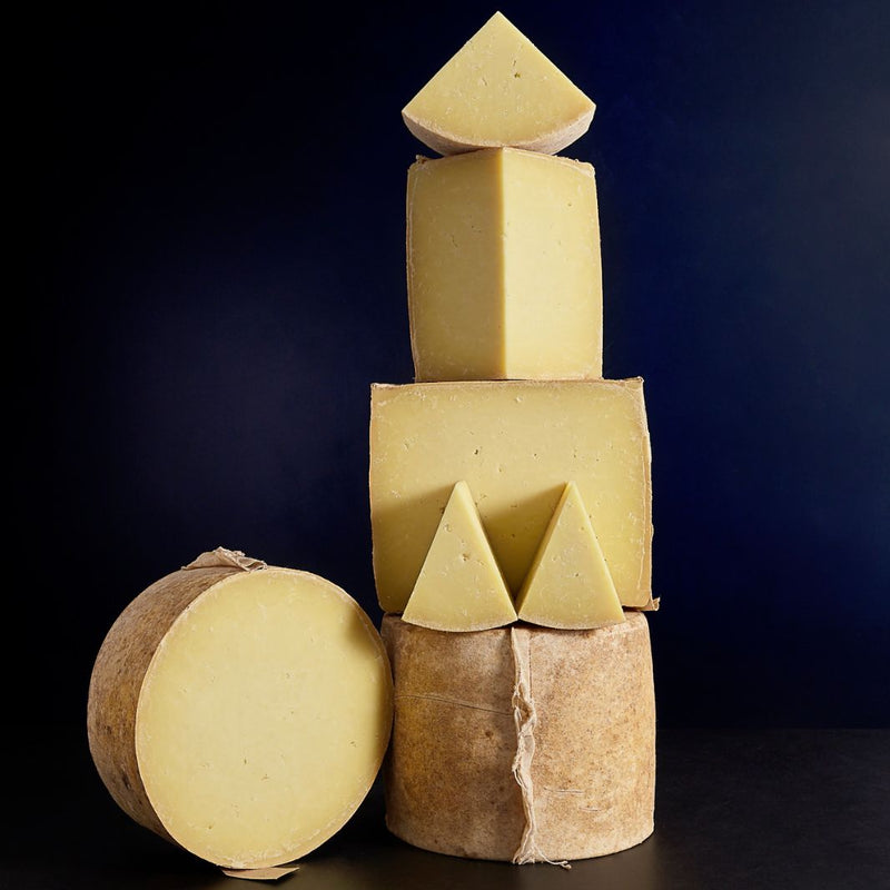 Tower of whole and various sized cut pieces of clothbound Corra Linn sheep’s milk cheese with creamy, succulent paste