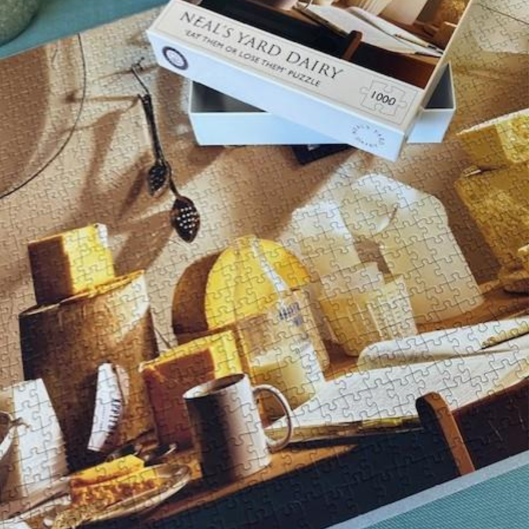 Jigsaw puzzle with completed sections and a box labeled 'Neal's Yard Dairy' on top.