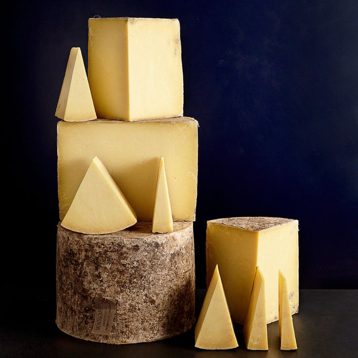Tower of whole and smaller cut pieces of cloth-bound Montgomery's Cheddar cheese with a firm but friable paste