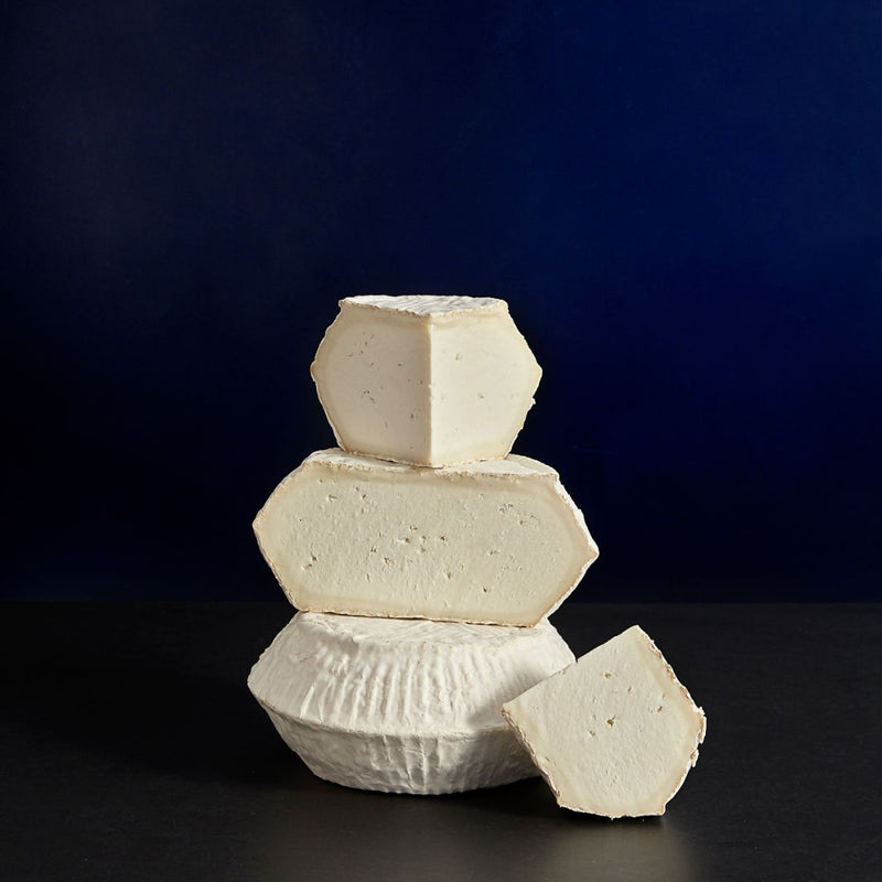 Tower of whole and various sized cut pieces of Ticklemore vegetarian goat’s cheese showing the bloomy, natural rind and white, chalky paste