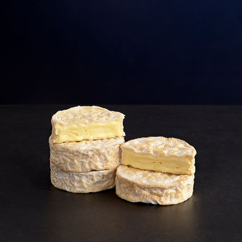 Small stacks of whole and cut Camembert-style Tunworth cheeses with a soft rind, and creamy, oozing, unctuous paste