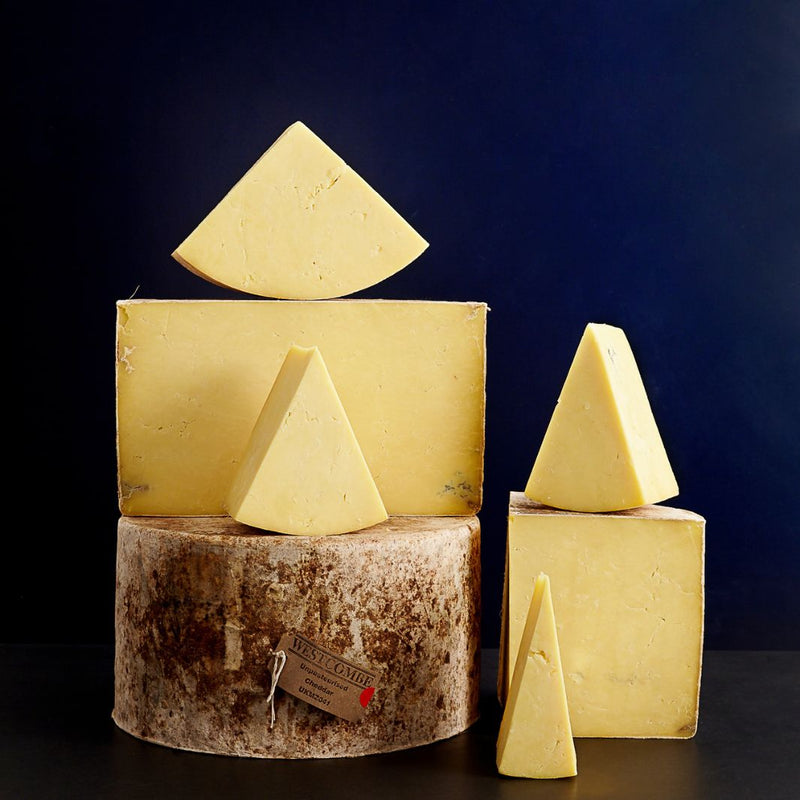 Tower of whole and smaller cut pieces of cloth-bound Westcombe Cheddar cheese with a soft, golden-coloured paste